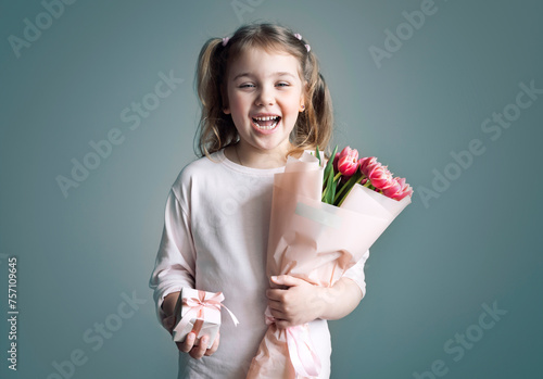 Child girl holding flowers bouquet and gift box loughing portrait on blue background. Spring promotional design card. Mother's day.Women's day. Greeting concept.