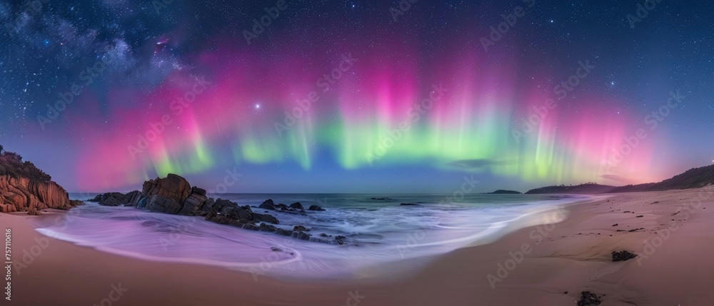 Aurora Australis. Spectacular Display of Vibrant Green and Pink Lights Painting the Night Sky Above an Australian Beach. Stars Twinkle as Waves Gently Caress the Rocky Shoreline.