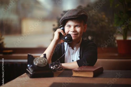 Smiling boy in a cap chatting on a classic rotary phone photo