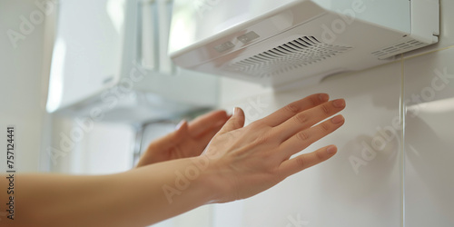 Frau auf öffentlicher Toilette trocknet sich die Hände unter elektrischem Händetrockner photo