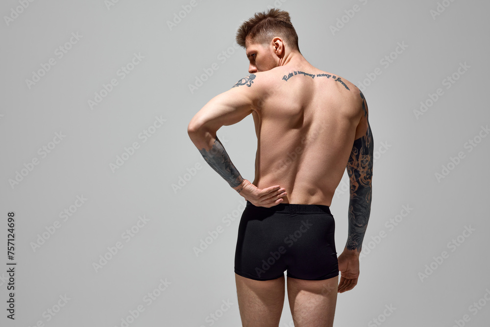 Rear view portrait of man holding hands behind back showing his spine against grey studio background. Copy space. Concept of natural beauty, fashion and style, male health and body care. Ad