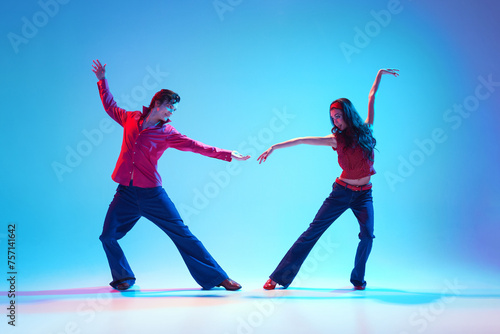 Stylish handsome young man and beautiful woman dancing rock and roll retro dance against blue background in neon light. Concept of hobby  dance class  party  50s  60s culture  youth