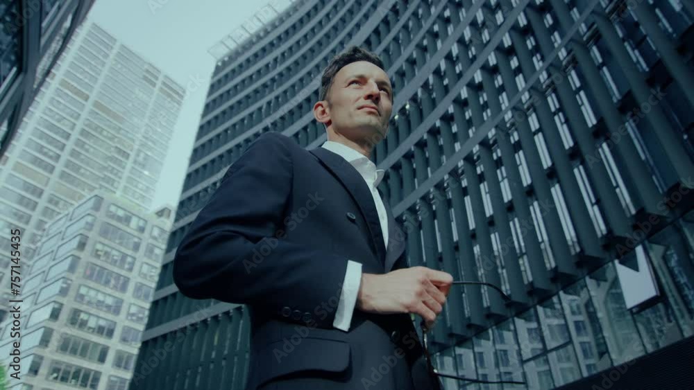 Elegant Handsome Caucasian Man Standing Outdoors In Suit and Glasses In Hand, Low Angle Elegant Handsome Caucasian Man Standing Outdoors In Suit and Glasses In Hand, Low Angle