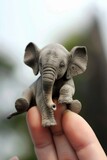 A small elephant sits on a man's finger