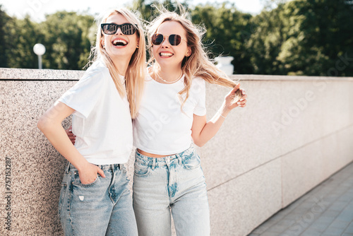 Two young beautiful smiling hipster female in trendy summer white top and jeans clothes. Carefree women posing in the street. Positive models having fun outdoors. Cheerful and happy. In sunglasses