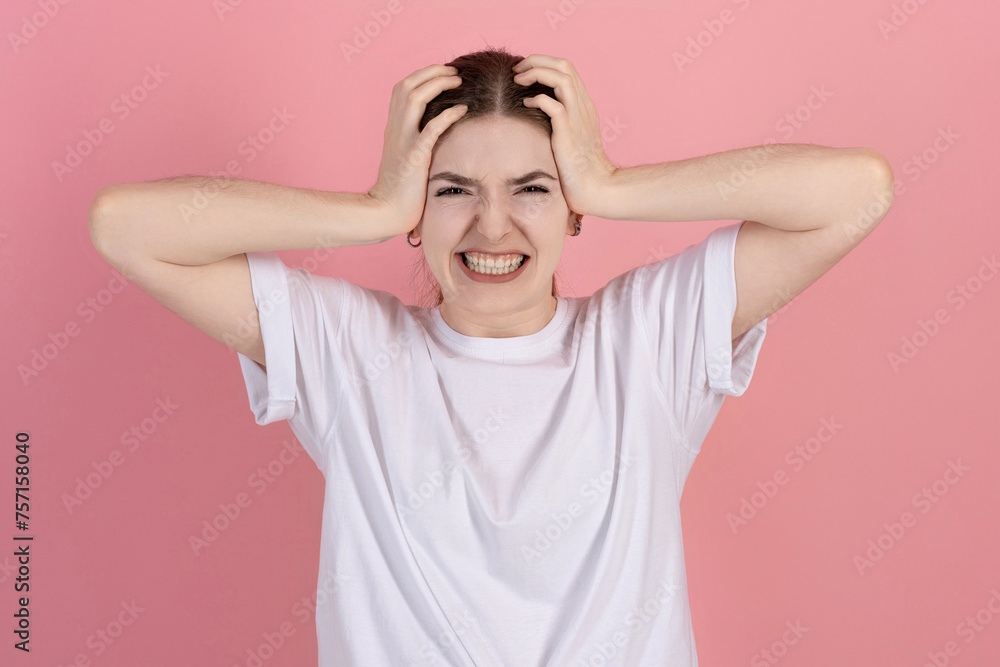 Angry attractive Caucasian young brunette woman in casual white t-shirt looks at camera with clenched teeth isolated on pink studio background. Angry attractive Caucasian young brunette woman in casual white t-shirt looks at camera with clenched teeth isolated on pink studio background.