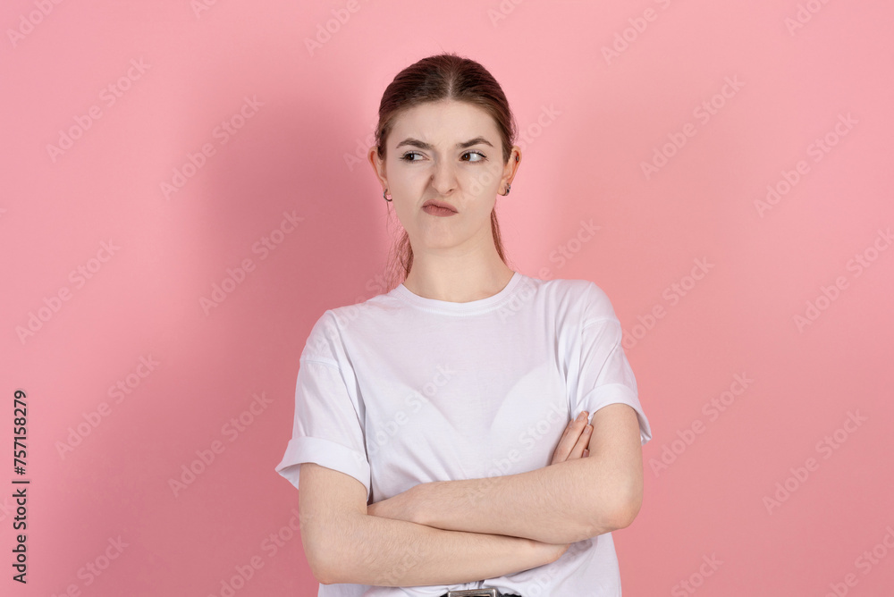 Portrait of a sad brunette girl, Caucasian young woman in a casual white t-shirt with arms crossed, sulking and frowning with disappointed isolated on a pink studio background. Portrait of a sad brunette girl, Caucasian young woman in a casual white t-shirt with arms crossed, sulking and frowning with disappointed isolated on a pink studio background.
