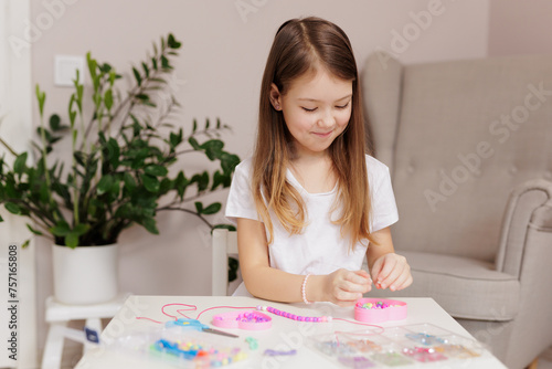 Happy girl making beaded jewelry at table in room