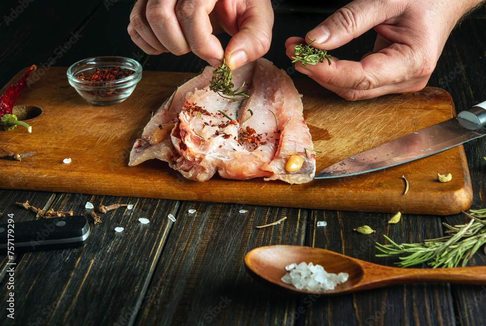 The cook adds aromatic rosemary to fresh fish fillets with his hands. A low-key concept for preparing a national fish dish according to a unique old recipe