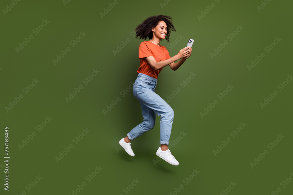 Full length photo of excited cute woman wear t-shirt jumping chatting instagram twitter telegram facebook isolated green color background