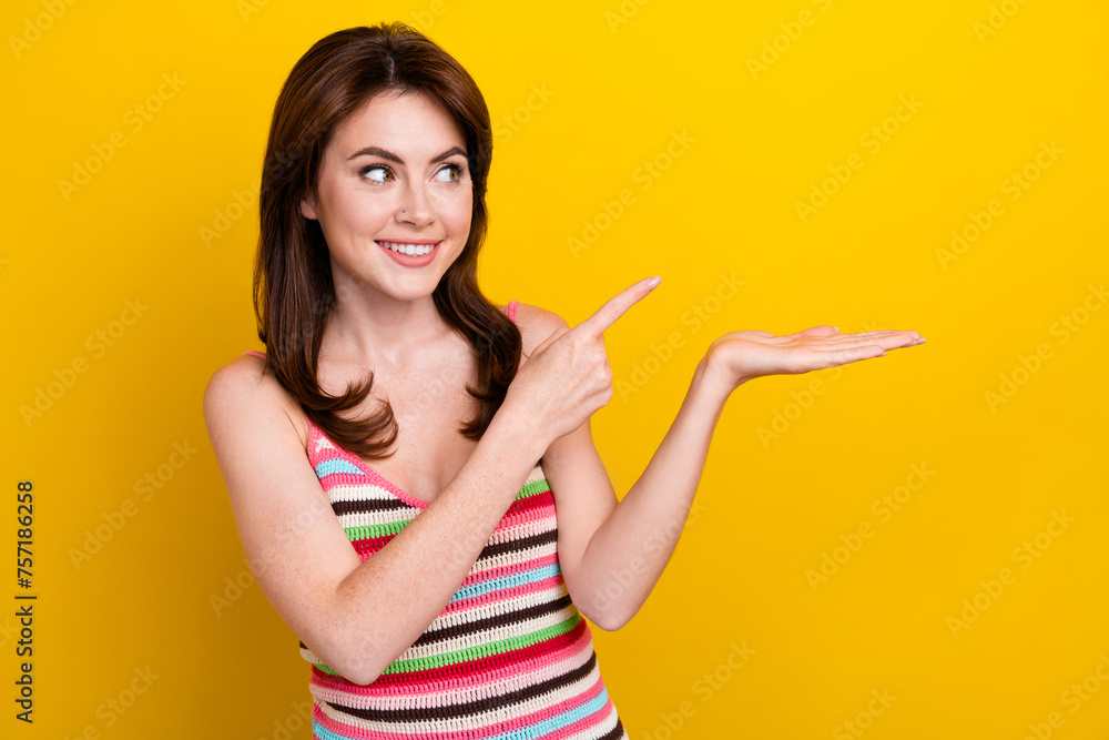 Portrait of cute woman with piercing wear tank look indicating at product on arm empty space isolated on vivid yellow color background Portrait of cute woman with piercing wear tank look indicating at product on arm empty space isolated on vivid yellow color background