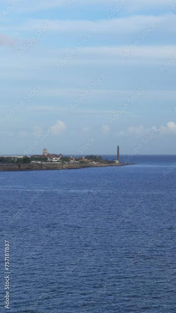 The coast of Meloneras in the Canary Islands with calm ocean and the Faro de Maspalomas on background The coast of Meloneras in the Canary Islands with calm ocean and the Faro de Maspalomas on background