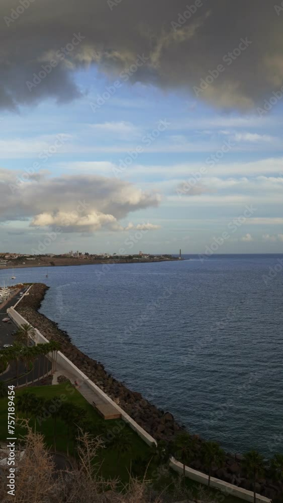 The coast of Pasito Blanco in the Canary Islands with calm ocean and the Faro de Maspalomas on background