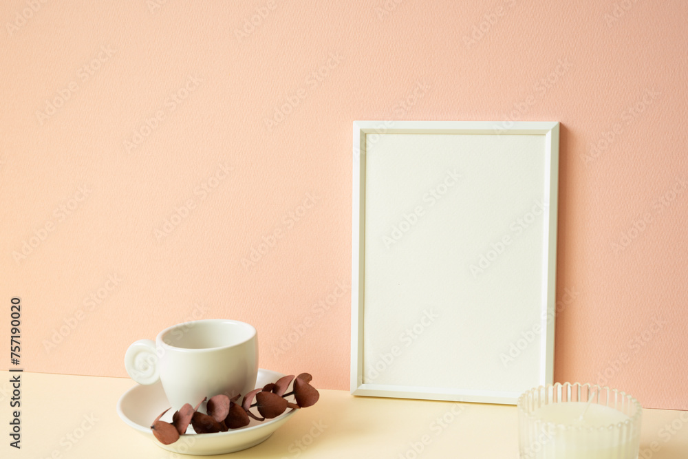 White blank picture frame with coffee cup, candle on ivory table. pink wall background