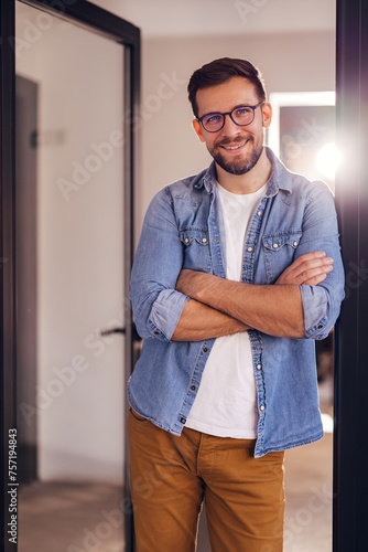 Young confident entrepreneur standing in modern office smiling and looking at camera.