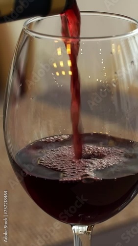 Close up of hand pours dry red wine from bottle into glass in restaurant. French wine. Drink. Vertical shot