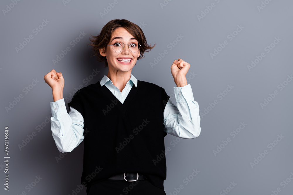 Photo of cheerful lucky woman ceo wear black waistcoat spectacles rising fists empty space isolated grey color background Photo of cheerful lucky woman ceo wear black waistcoat spectacles rising fists empty space isolated grey color background