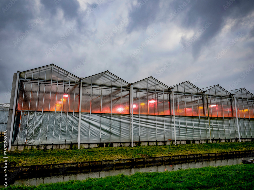 Greenhouse glowing warmly against a dramatic evening sky Greenhouse glowing warmly against a dramatic evening sky