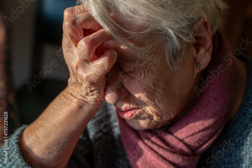 Elderly woman in contemplation, hand to forehead in a softly lit room. photo