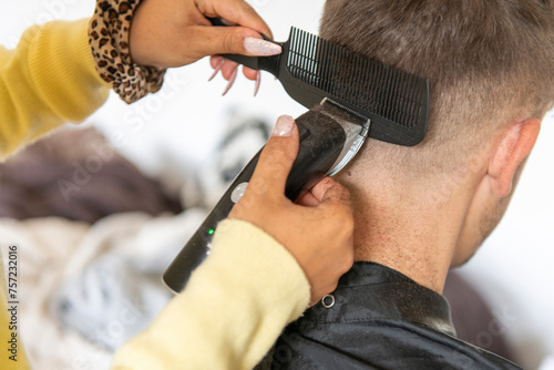 A person is receiving a haircut from a hairstylist using electric clippers and a comb. photo
