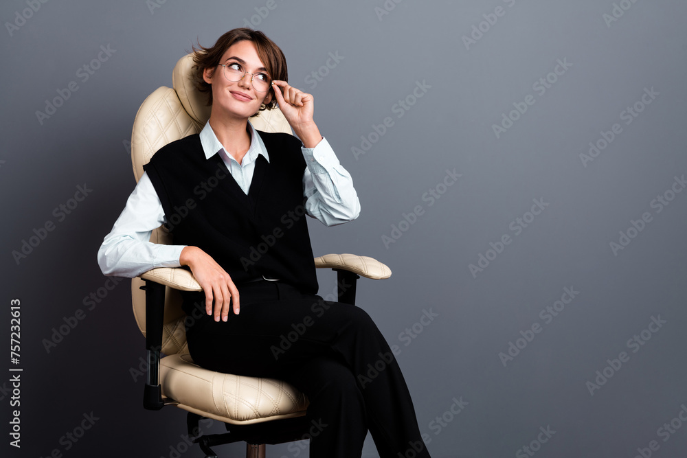 Photo of smart nice woman wear black waistcoat touch glasses in armchair look at offer empty space isolated on gray color background Photo of smart nice woman wear black waistcoat touch glasses in armchair look at offer empty space isolated on gray color background
