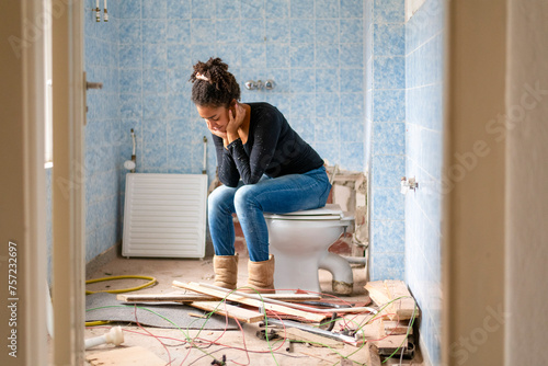 A woman takes a break on a toilet amidst a chaotic bathroom renovation. photo