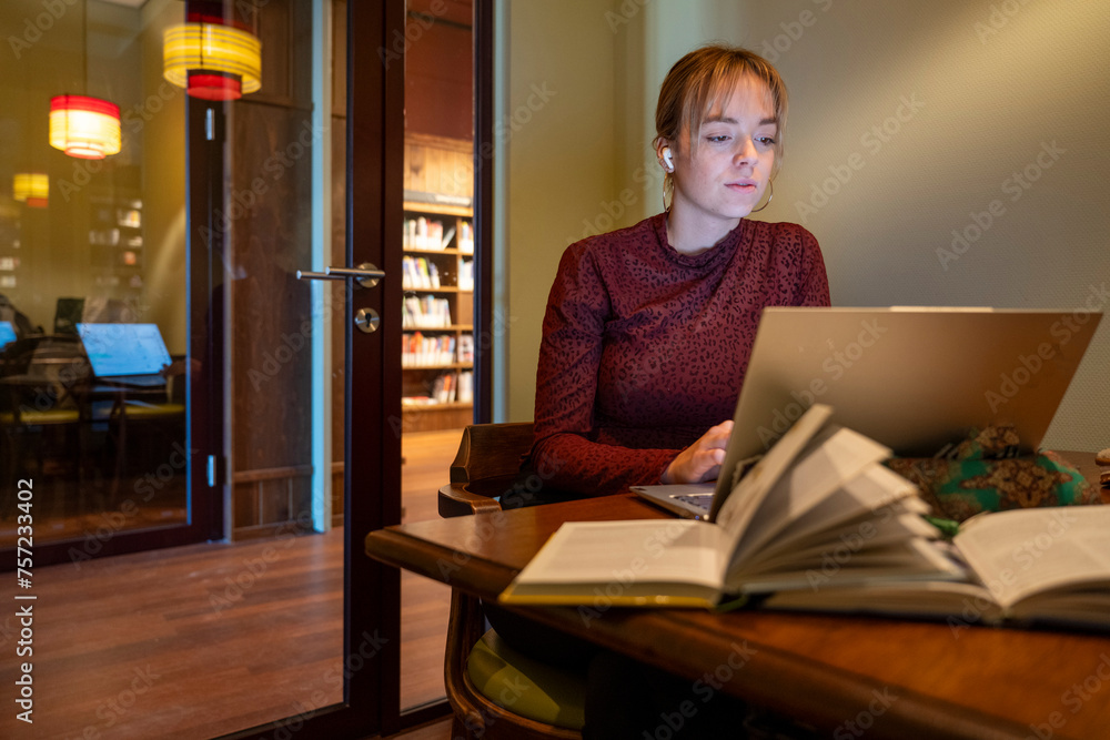 Focused individual studying at a cozy library corner with a laptop and books. Focused individual studying at a cozy library corner with a laptop and books.