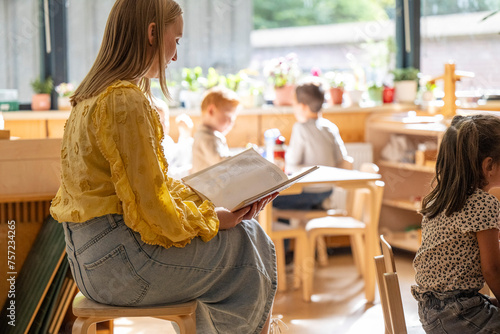 Young woman reading a book in a sunny caf with children nearby. photo