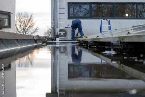 Worker repairs a rooftop on a clear day, reflected in standing water. photo