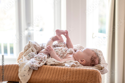 Baby lying playfully on a wicker daybed by the window. photo