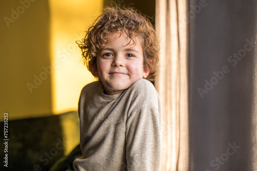 A playful child peeking from behind a curtain with a warm smile. photo