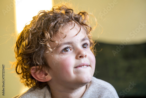 Young child with curly hair looking up thoughtfully in a warmly lit room. photo