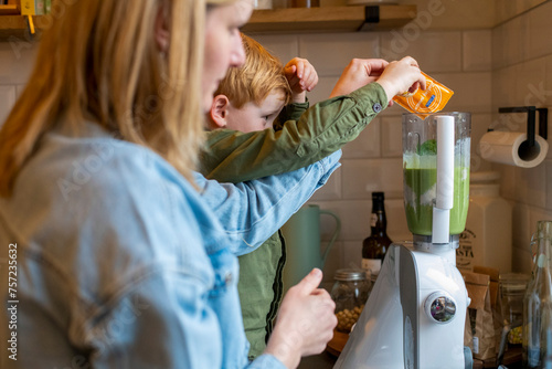 A child is helping pour ingredients into a blender guided by an adult in a home kitchen setting. photo