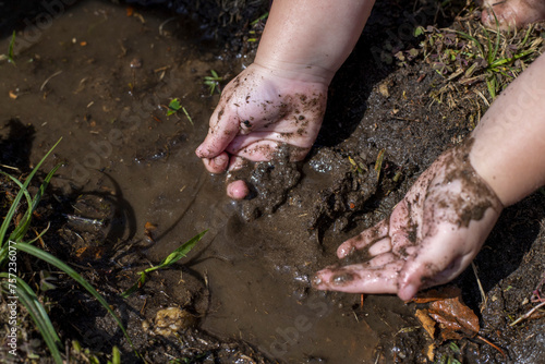 Child's hands covered in mud by a puddle photo