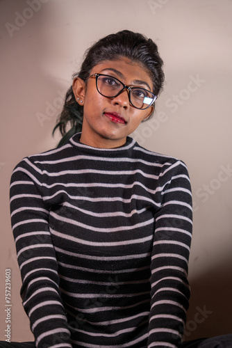 A woman wearing glasses and a striped shirt is sitting on a chair. She has a serious expression on her face
