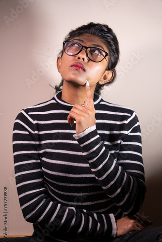 A woman with glasses is sitting on a wooden chair and looking at the camera. She is wearing a striped shirt and has a cigarette in her mouth. Concept of contemplation and introspection