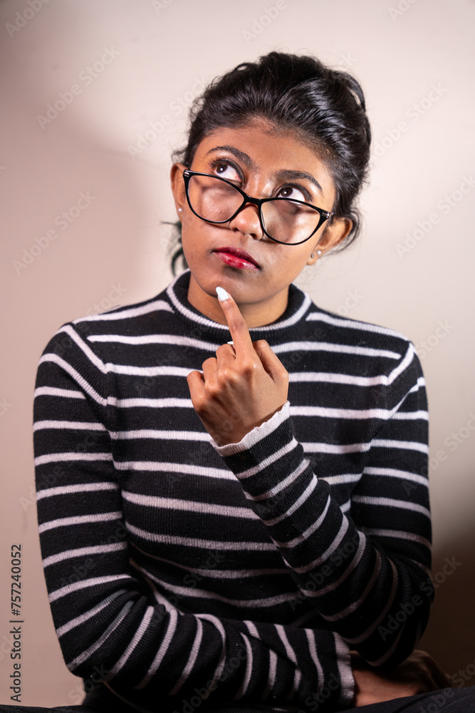 A woman with glasses is looking at something and her hand is on her chin. She is wearing a striped shirt A woman with glasses is looking at something and her hand is on her chin. She is wearing a striped shirt