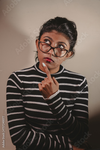 A woman with glasses is looking at something and pointing her finger. She is wearing a striped shirt and has a red lipstick on. Concept of curiosity and contemplation