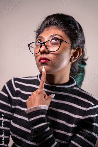A woman with glasses and red lipstick is looking down and pointing to her nose. She is wearing a striped shirt and has a green bird on her hair. Concept of curiosity and contemplation
