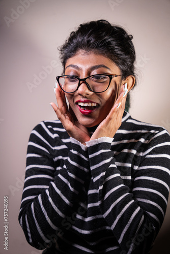 A woman with glasses and red lipstick is making a surprised face. She is wearing a striped shirt and has a pair of earbuds in her ears © oybekostanov