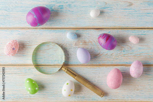 Top view of a magnifying glass  next to colorful, textured eggs on a rustic wooden surface. Easter eggs hunting and search