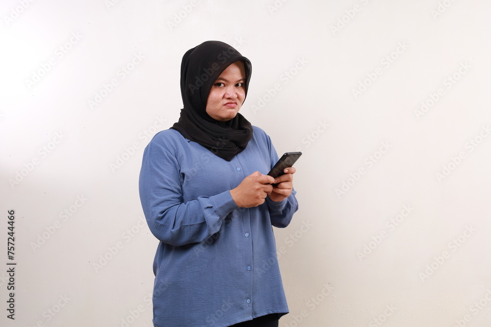 Unhappy asian adult woman standing while holding a cell phone Unhappy asian adult woman standing while holding a cell phone