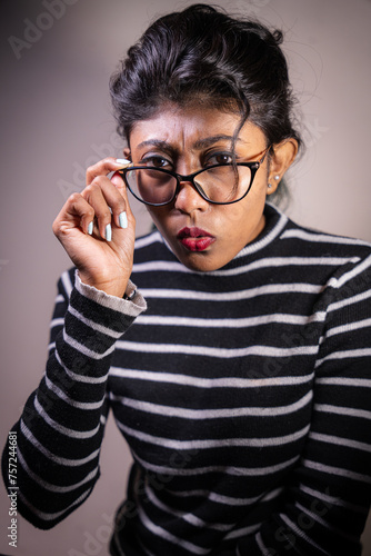 A woman with glasses and a red lip is wearing a striped shirt. She is looking at the camera with a surprised expression