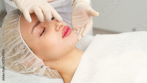 Injection procedure for lip augmentation, close-up. The cosmetologist slowly and carefully injects filler into the client’s lips. Advertising concept for facial care, youth and beauty.