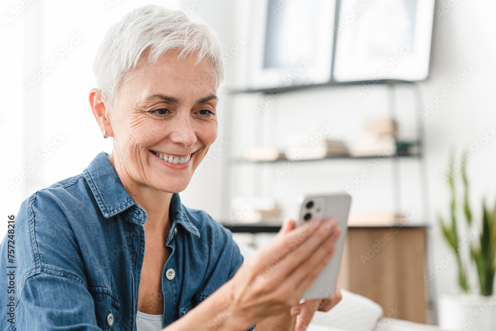 Closeup shot of mature Caucasian female housewife using cellphone for ordering delivery online from home. Middle-aged woman doing remote shopping on webpages