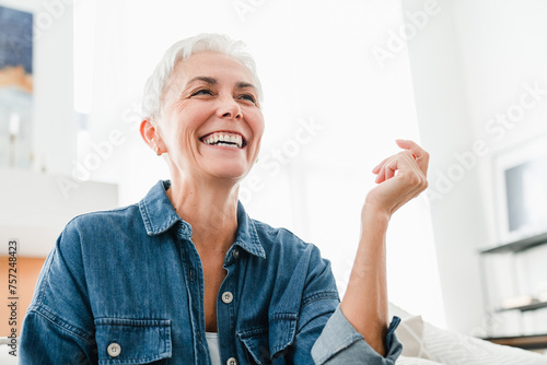 Smiley Caucasian mature woman laughing sitting on the couch. Happy middle-aged woman having positive mood attitude to life relaxing at home indoors. photo