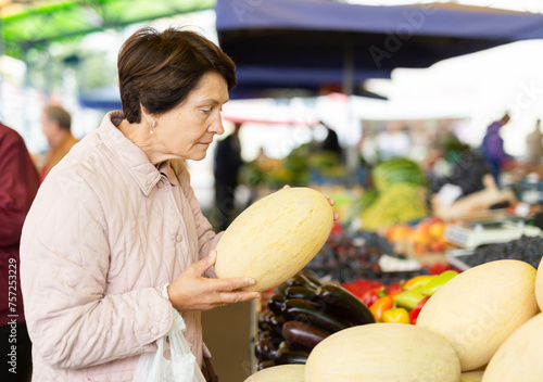 Elderly woman buys a melon at an open air market