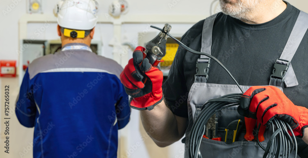 Fototapeta premium Focused Electrician Holding Cable Stripping Tool with Partner in Background