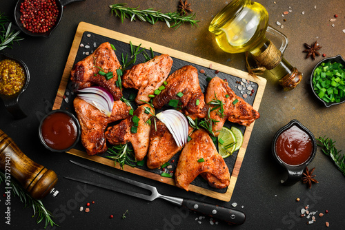 Fried chicken wings with onions and spices on a slate board. On a dark background. photo