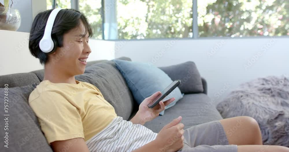 Teenage Asian boy enjoys music with white headphones, holding a smartphone with copy space Teenage Asian boy enjoys music with white headphones, holding a smartphone with copy space